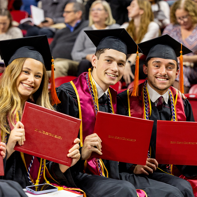 Three students pose with their diplomas at commencement