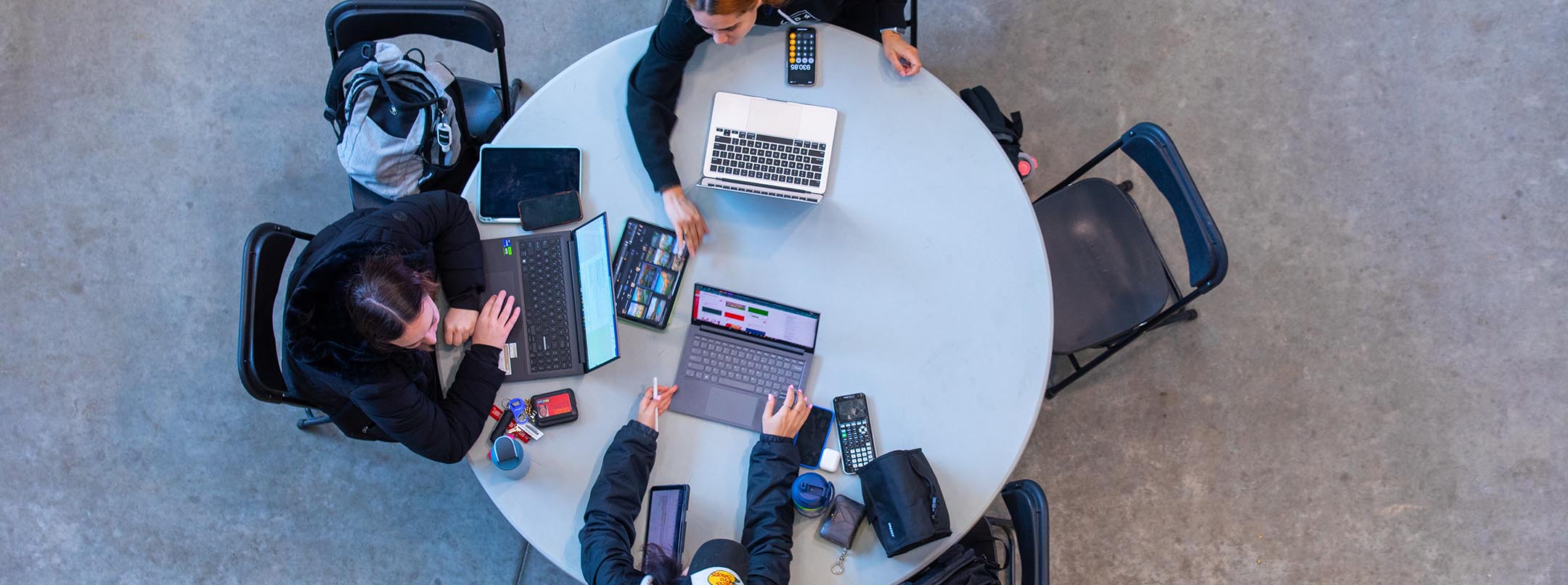 Overhead view of a round table with three students working together on laptops.