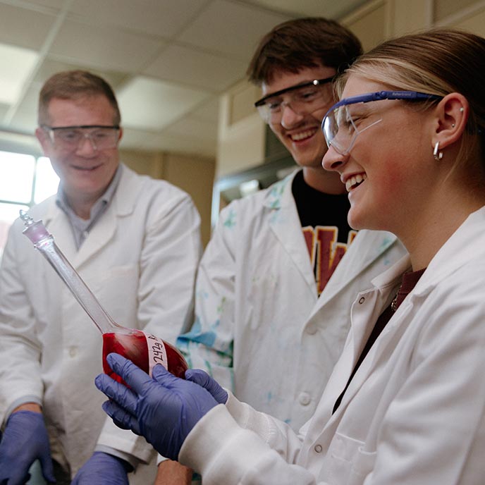 Two students and an instructor observe a liquid sample in a research lab.