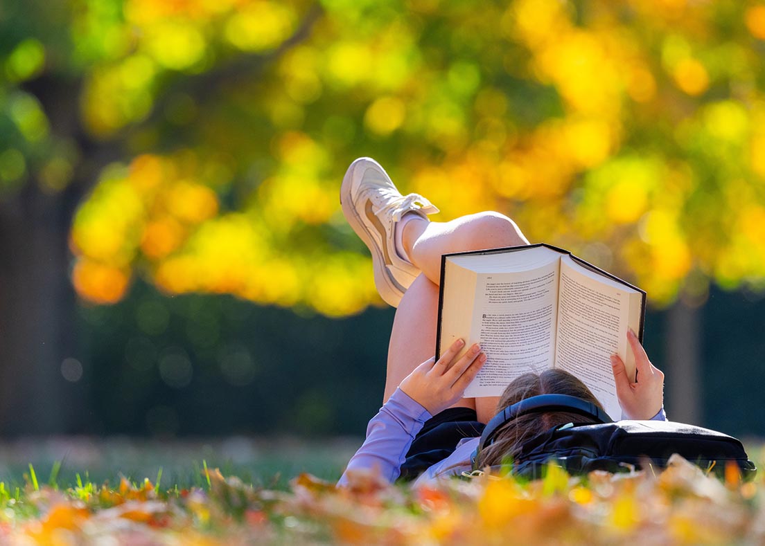 A student reading a book while laying on central campus.