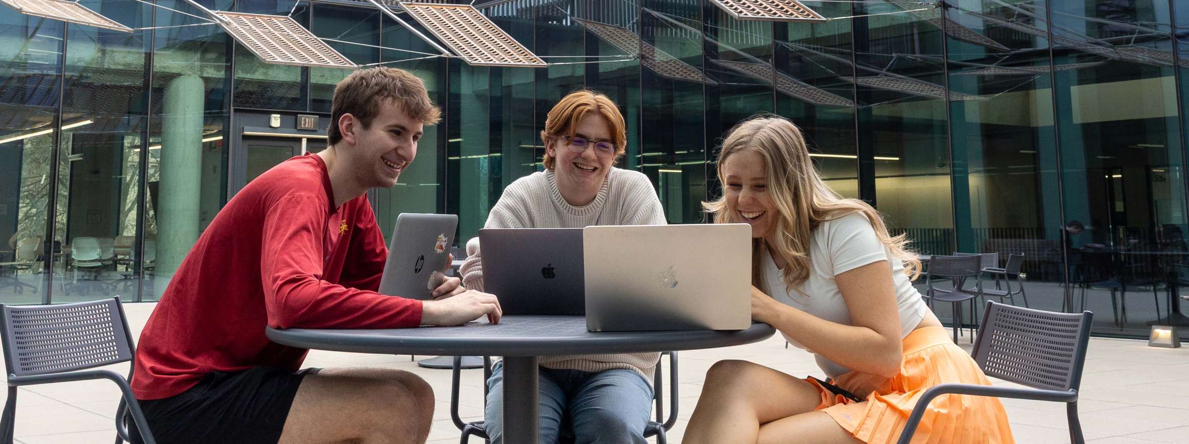 Three students working on computers in the Student Innovation Center courtyard